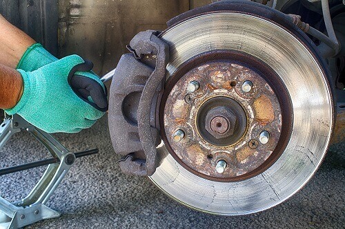Brake Repair in Columbia, MD | Columbia Auto Care & Car Wash. Close-up image of a car mechanic’s hand working on a brake rotor and brake pad.