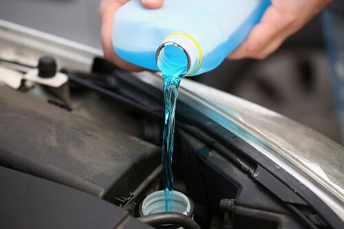 Fluid Services in Columbia, MD | Columbia Auto Care & Car Wash. Close-up image of a mechanic pouring blue coolant from a canister into a car engine.