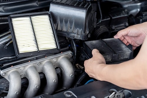 Tune-ups in Columbia, MD | Columbia Auto Care & Car Wash. Image of mechanic’s hand holding an old engine air filter and changing into a new filter as part of car tune-up.
