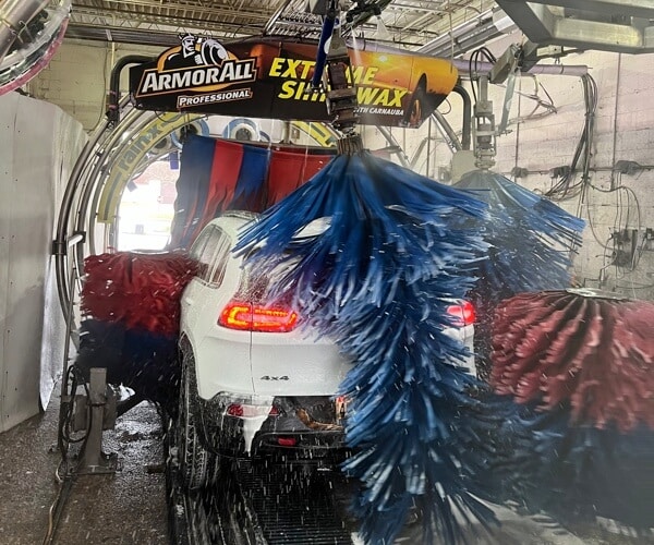 monthly car wash subscription for Columbia Car Wash in Columbia Md, image of white jeep cherokee driving through car wash with red and blue brushes scrubbing all around vehicle with Armorall sign above it