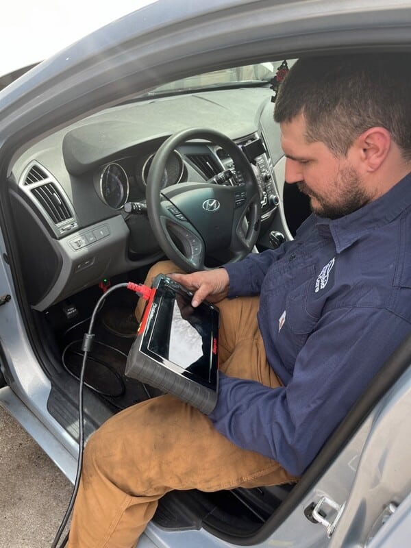 ASE certified mechanic that works at Columbia Auto Care in Columbia MD sitting in driver's side of car with shops computer diagnostic tool running a scan