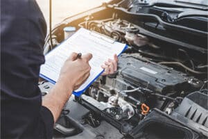 Mechanic checking a car engine with inspecting writing to the clipboard the checklist for repair machine, car service and maintenance.