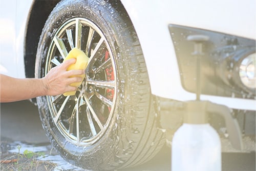 A man is holding a sponge and cleaning his car’s wheel.